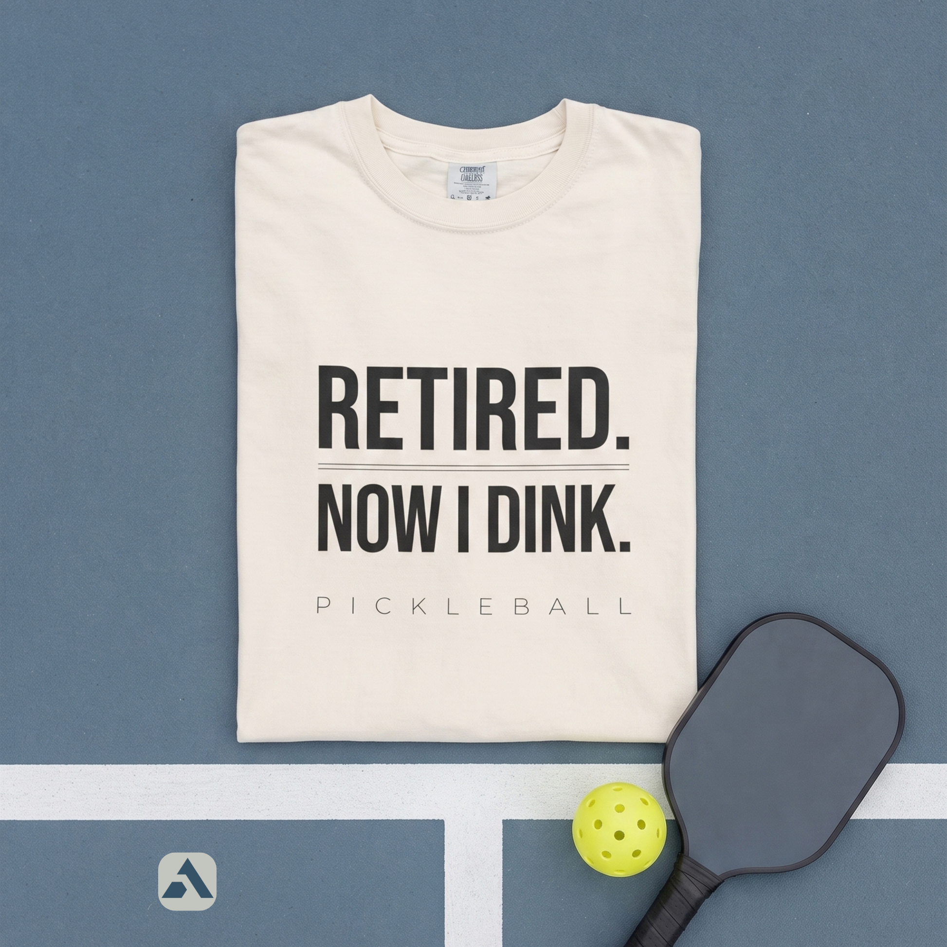 Retired. Now I Dink. pickleball t-shirt, Ivory — folded flat-lay with paddle
